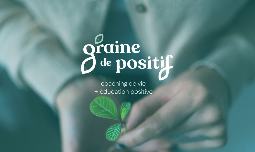 Logo "Graine de positif - coaching de vie + éducation positive" blanc, sur une photographie en gros plan de main tenant un trèfle vert.